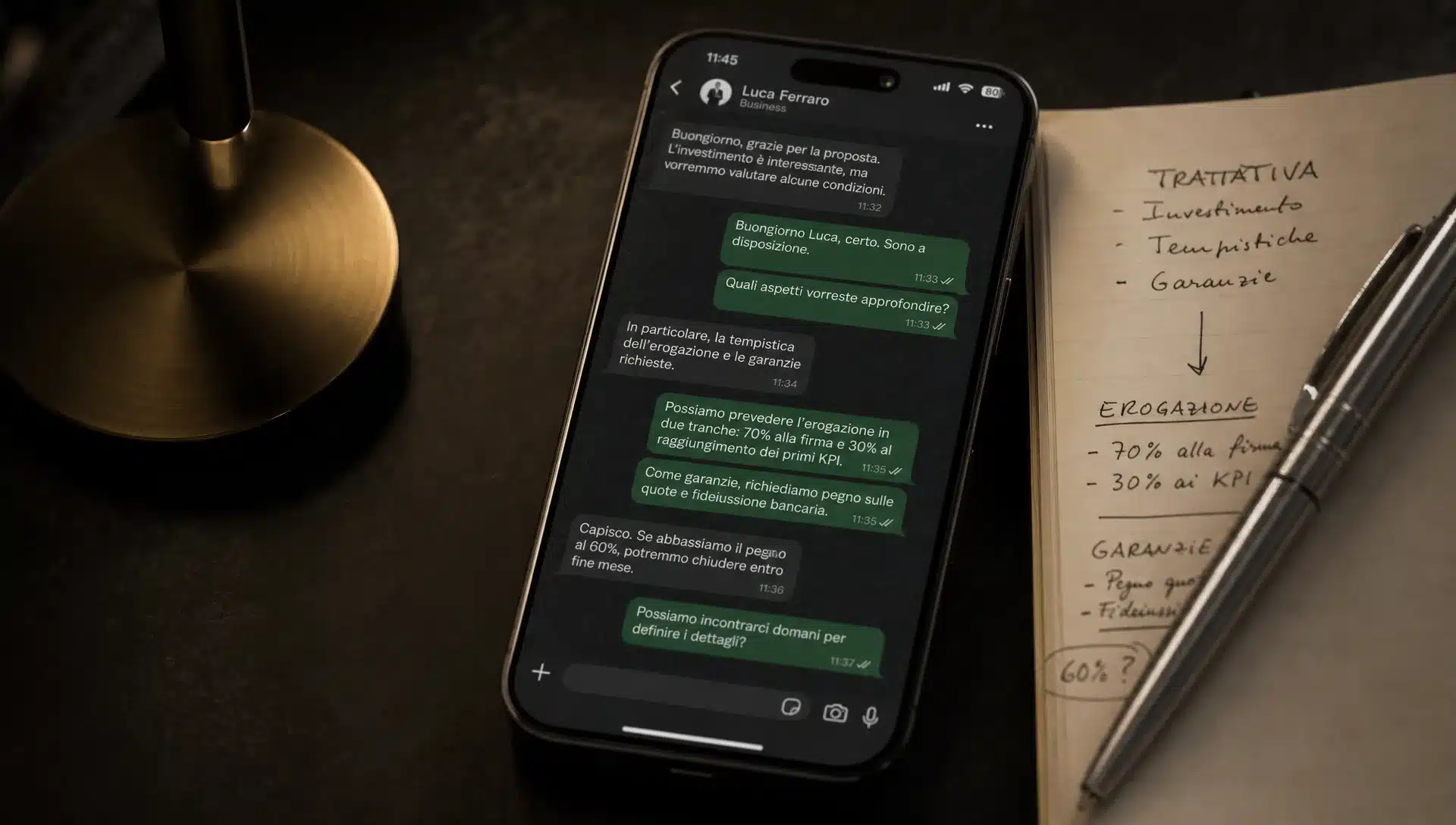 Uno smartphone con una chat di WhatsApp Business aperta accanto a un taccuino e una penna, su una scrivania da trattativa.