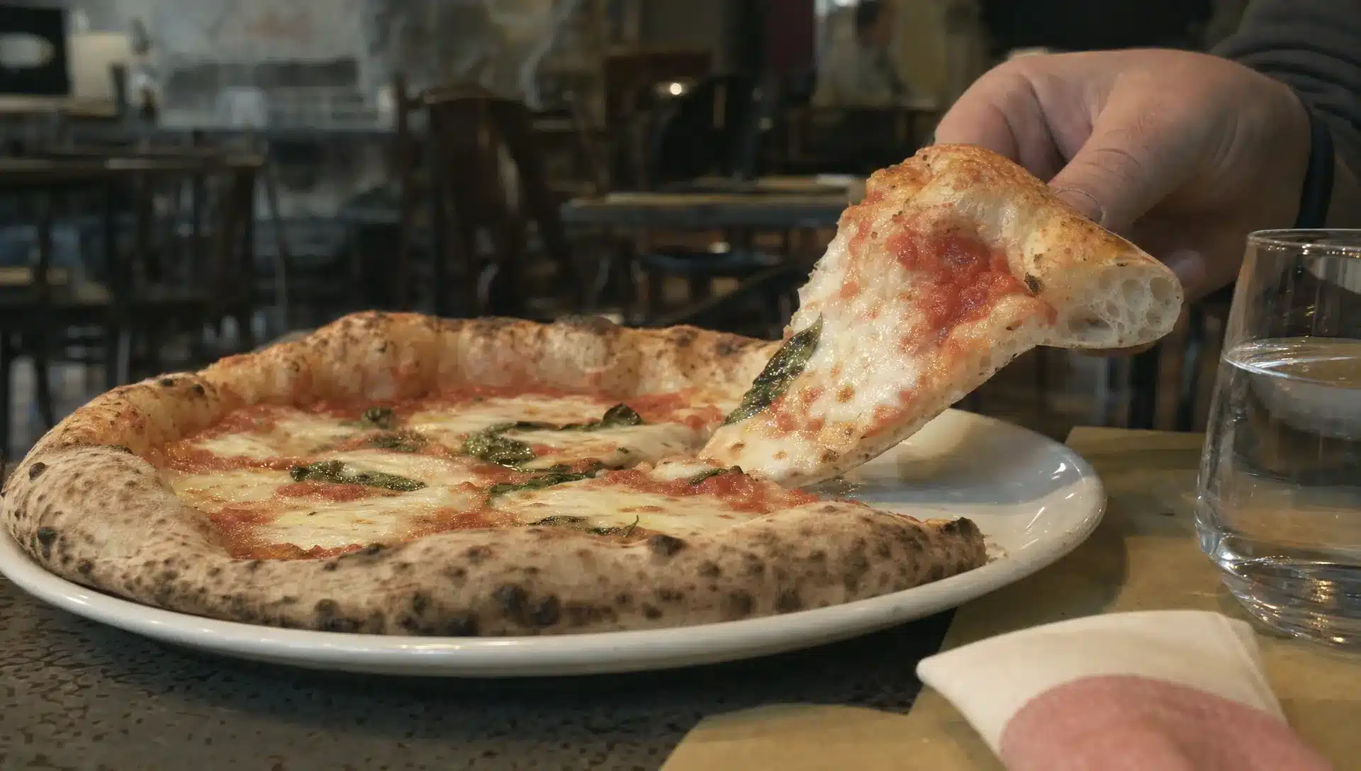 Una fetta sollevata lascia vedere la sezione dell’impasto e la crosta di una pizza appena servita al tavolo.